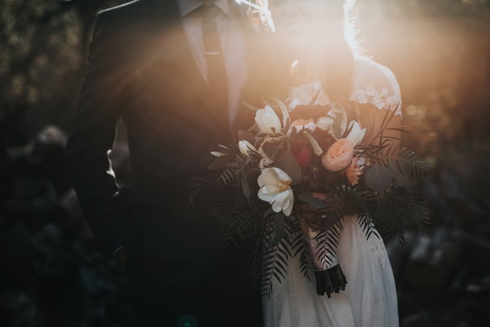 Couple de mariés tenant un bouquet à la lumière dorée du soir